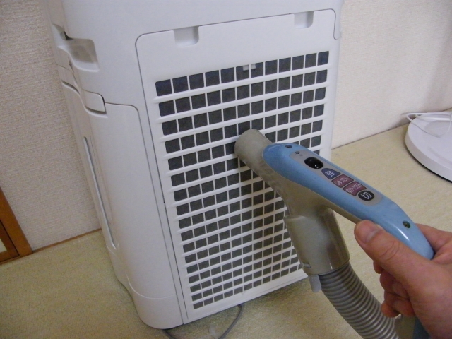 空気清浄機の吸気グリル部分をブラシで掃除している様子を撮影した写真です。