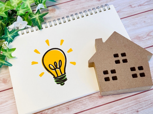家の模型と電球のイラストで電気料金の比較や節約をイメージ