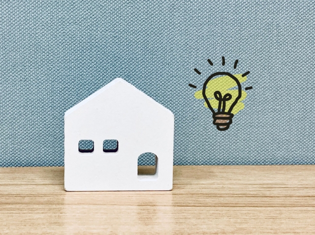 家の模型と電球のイラストで電気料金や省エネをイメージした写真