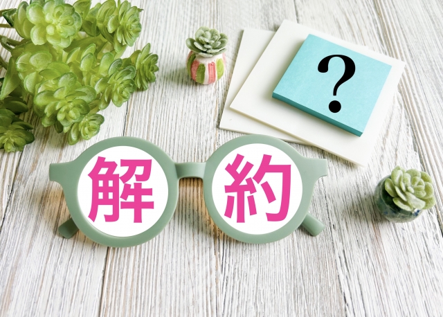 解約の文字が入ったメガネと疑問符カードの写真。固定電話や通信契約の解約を考えるイメージ。