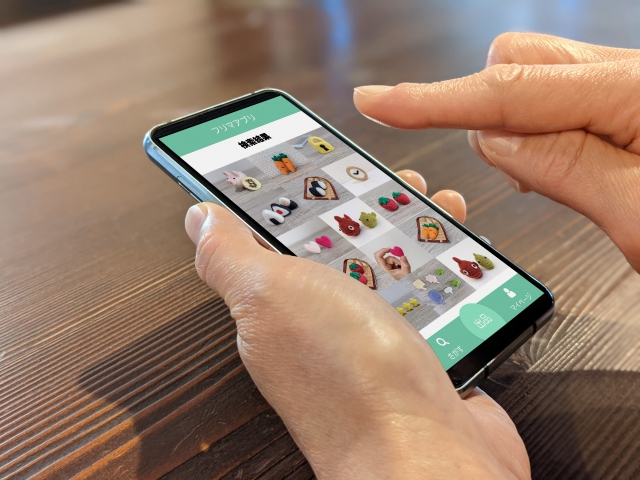 スマートフォンの画面で商品一覧を閲覧している手元の写真。買取アプリや宅配査定サービスを使うイメージ。