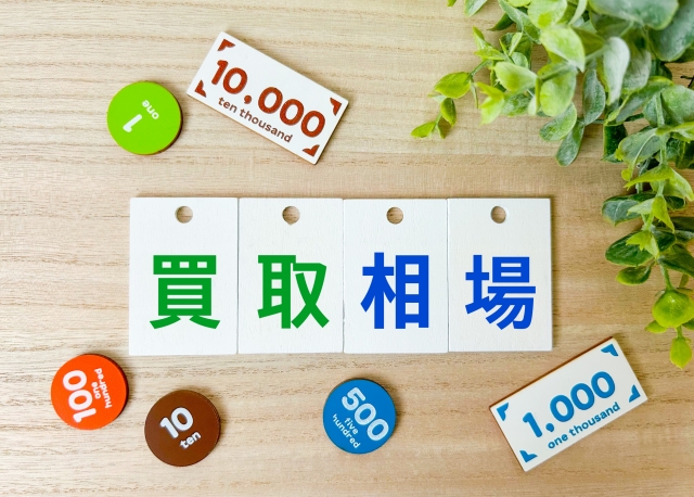 「買取相場」と書かれたカードと硬貨、葉、木製ボードが並ぶ写真。買取価格の目安や比較をイメージした構図。