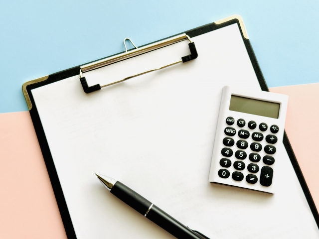 クリップボードとボールペン、電卓が並ぶ写真。買取金額の計算や査定作業をイメージした構図。